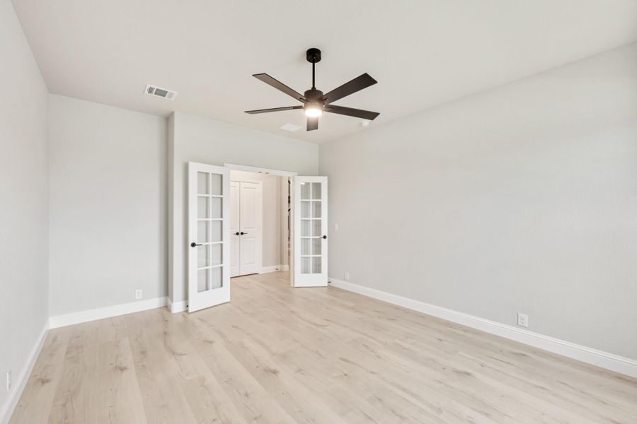 Empty bedroom with light hardwood floors, ceiling fan, and white French doors leading to closet