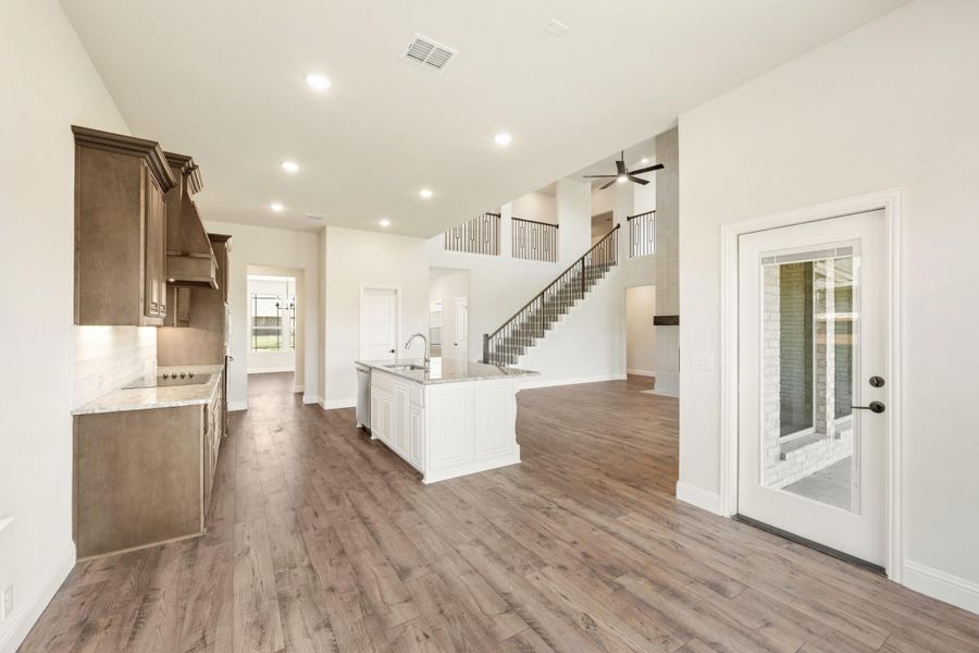 Open-concept kitchen with white island, dark wood cabinets, hardwood floors, and staircase leading to second floor