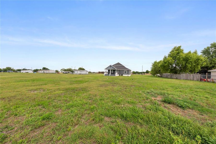 Expansive grassy lot with a detached residence featuring a covered front porch and a dark shingle roof