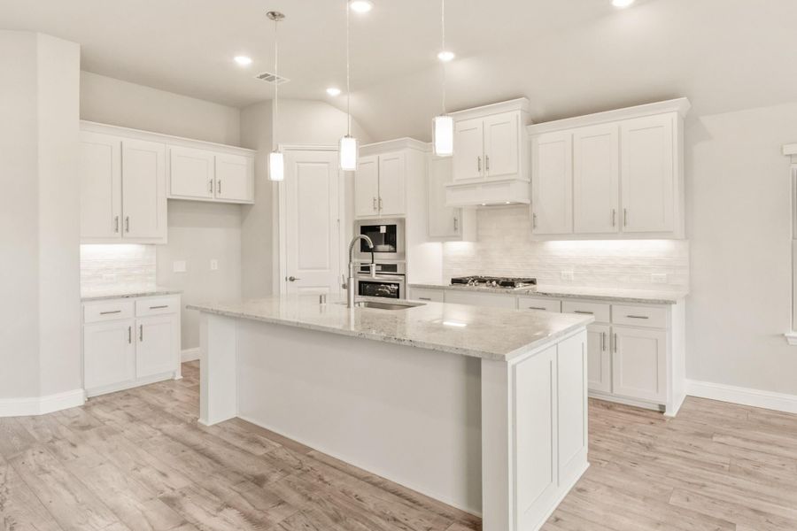 White kitchen with large center island, granite countertops, pendant lights, and light wood floors White kitchen with large center island, granite countertops, pendant lights, and light wood floors