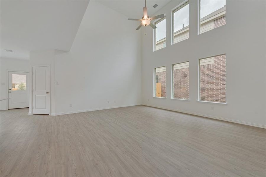 Unfurnished living room with a healthy amount of sunlight, ceiling fan, light wood-type flooring, and a high ceiling