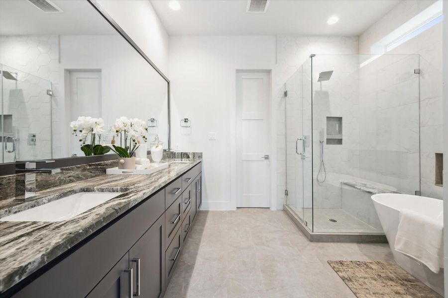 This modern bathroom features a spacious layout with a large marble-topped vanity, dual sinks, and ample storage. It includes a glass-enclosed shower, a freestanding bathtub, and elegant tile work, creating a luxurious and serene atmosphere.