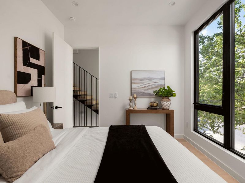 High ceilings and a massive window framing green views define this light-filled modern bedroom.