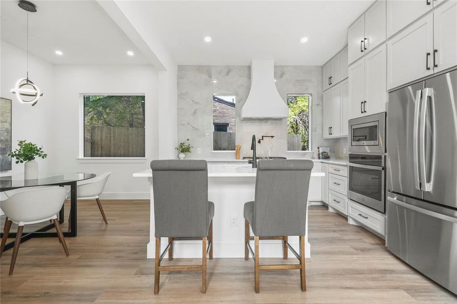 Kitchen with white cabinetry, decorative light fixtures, stainless steel appliances, recessed lighting, and light wood-style floors
