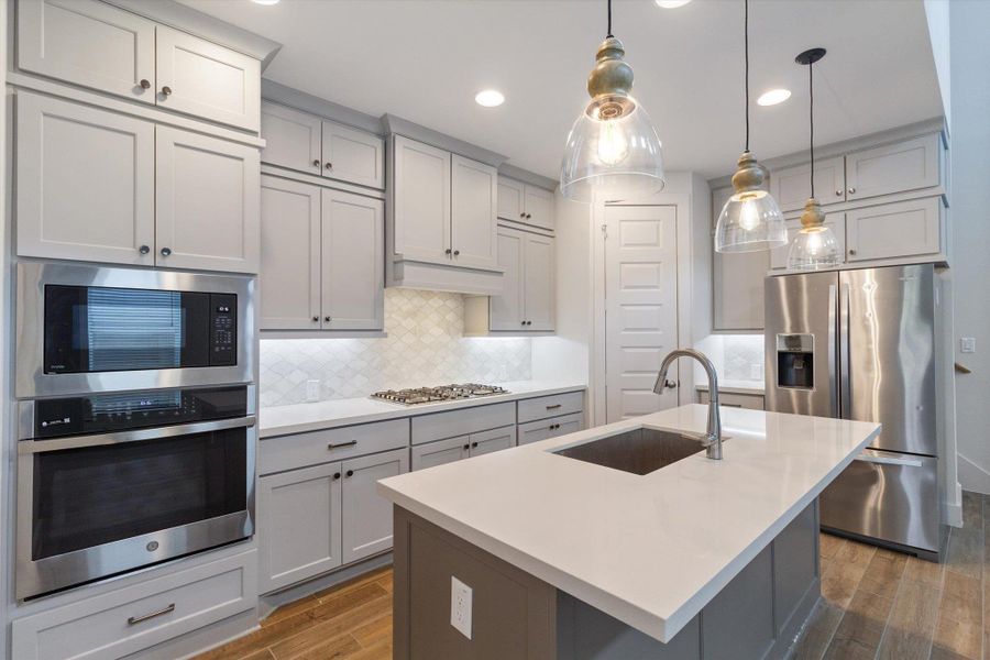 Kitchen featuring gray cabinets, stainless steel appliances, backsplash, pendant lighting, and dark wood finished floors