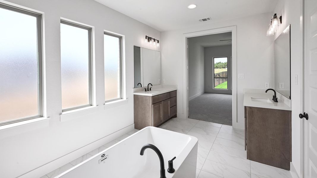 Bathroom with marble finish floors, a freestanding tub, and two vanities