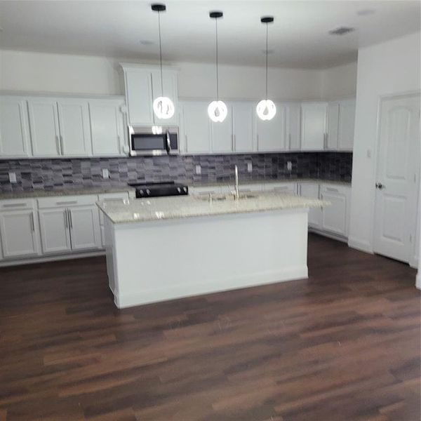 Kitchen with dark wood-type flooring, white cabinets, sink, and pendant lighting