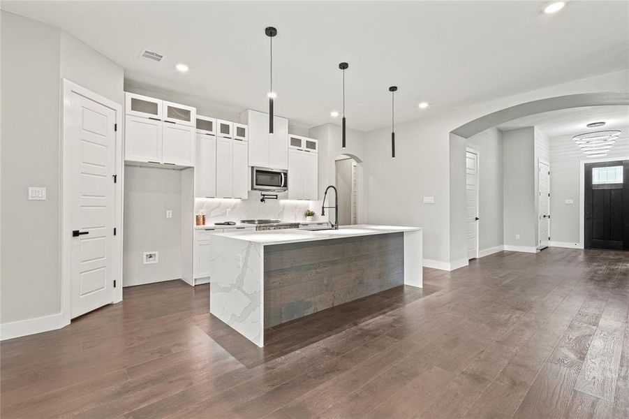 Kitchen featuring stainless steel microwave, arched walkways, recessed lighting, an island with sink, and dark wood-type flooring
