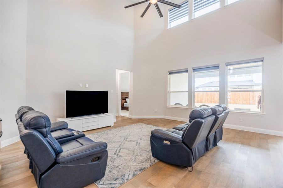 Living room featuring a ceiling fan, light wood-type flooring, a towering ceiling, and baseboards