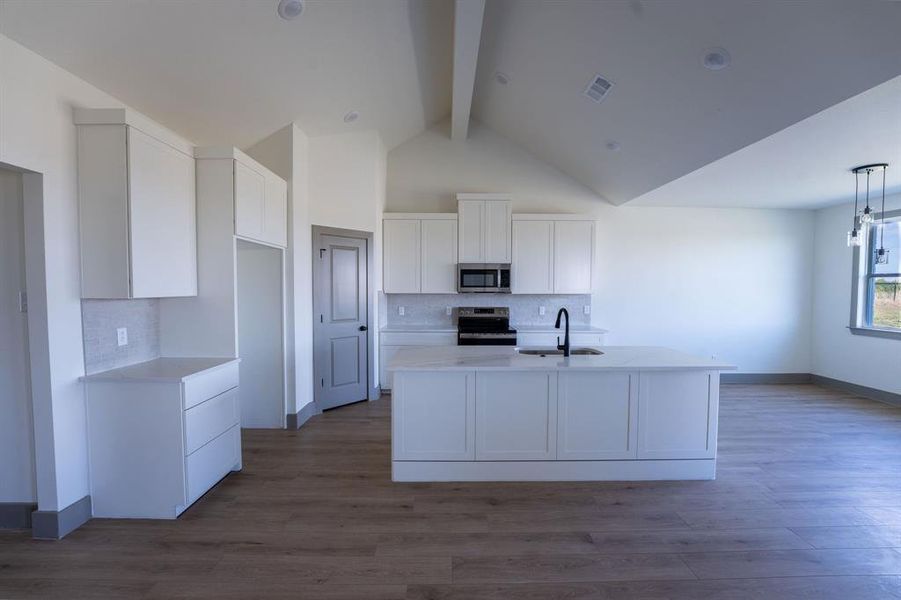 Kitchen featuring tasteful backsplash, beamed ceiling, white cabinetry, appliances with stainless steel finishes, and light stone counters Kitchen featuring tasteful backsplash, beamed ceiling, white cabinetry, appliances with stainless steel finishes, and light stone counters