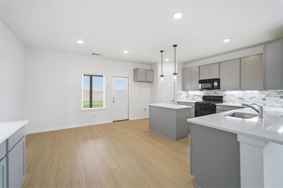 Kitchen featuring gray cabinets, black appliances, a center island, light wood-style flooring, and pendant lighting