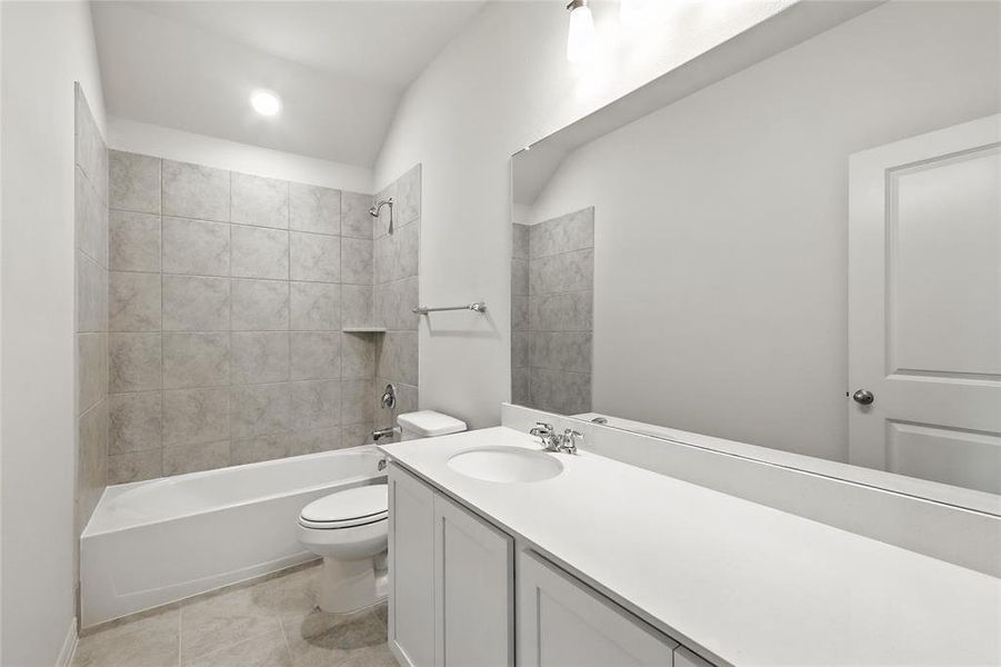 Bathroom featuring vanity, shower / tub combination, vaulted ceiling, and light tile patterned floors