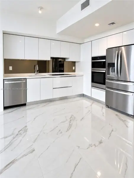 High-gloss flat-panel white cabinetry, stainless steel appliances, integrated double wall ovens, mirror-finish backsplash, and polished stone-finish tile flooring High-gloss flat-panel white cabinetry, stainless steel appliances, integrated double wall ovens, mirror-finish backsplash, and polished stone-finish tile flooring