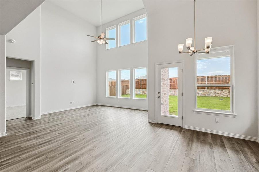 Unfurnished dining area with ceiling fan with notable chandelier, wood-type flooring, and a high ceiling