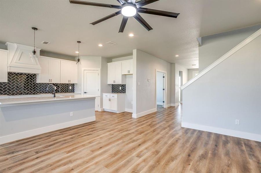 Kitchen with tasteful backsplash, pendant lighting, light wood-style floors, white cabinets, and premium range hood