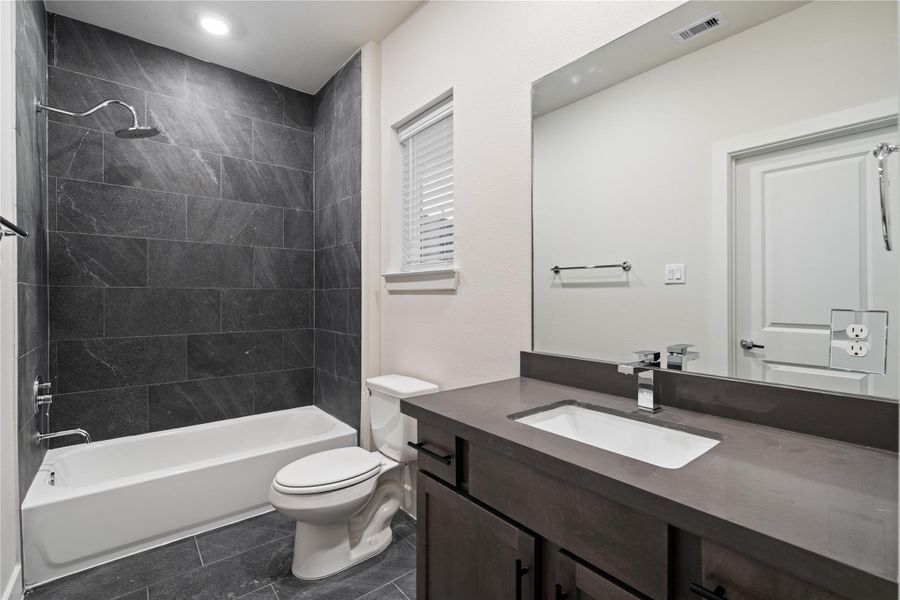 Secondary bathroom finished with full height dark tile surround and a clean, modern vanity.