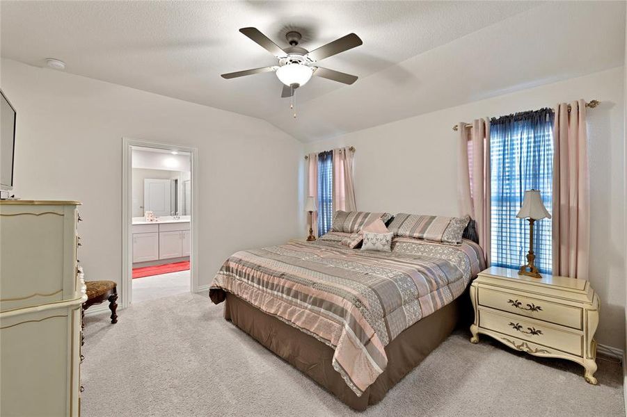 Bedroom with ensuite bathroom, light colored carpet, a ceiling fan, and vaulted ceiling