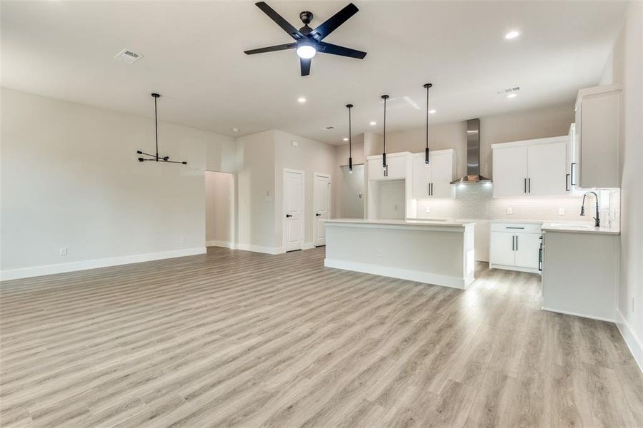 Kitchen featuring wall chimney range hood, light hardwood / wood-style floors, ceiling fan, white cabinetry, and a center island