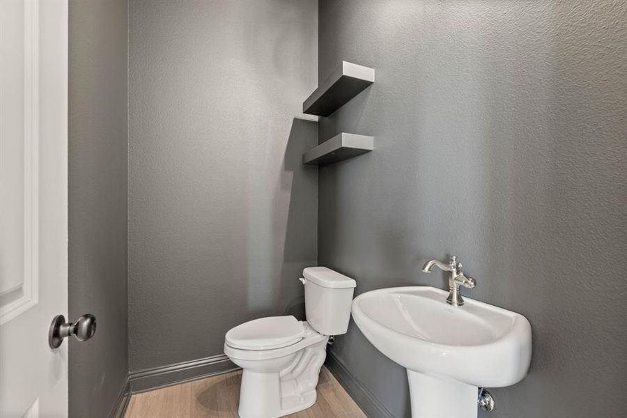 Bathroom with a textured wall, toilet, a sink, wood finished floors, and baseboards