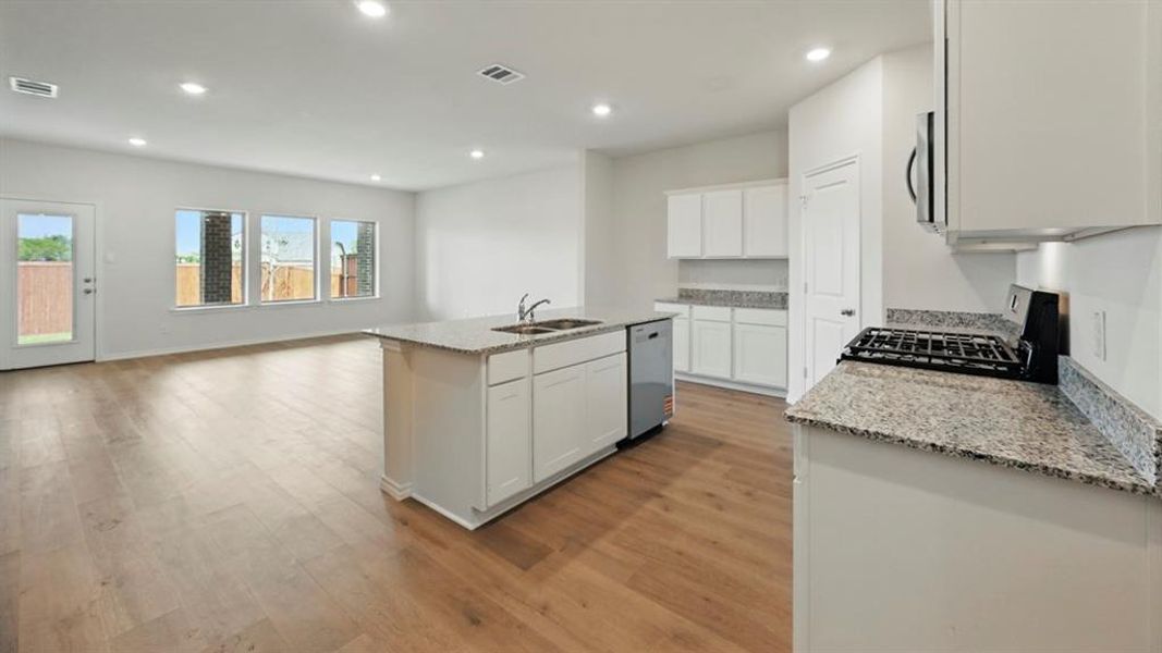 Kitchen with light stone countertops, appliances with stainless steel finishes, recessed lighting, an island with sink, and light wood-type flooring