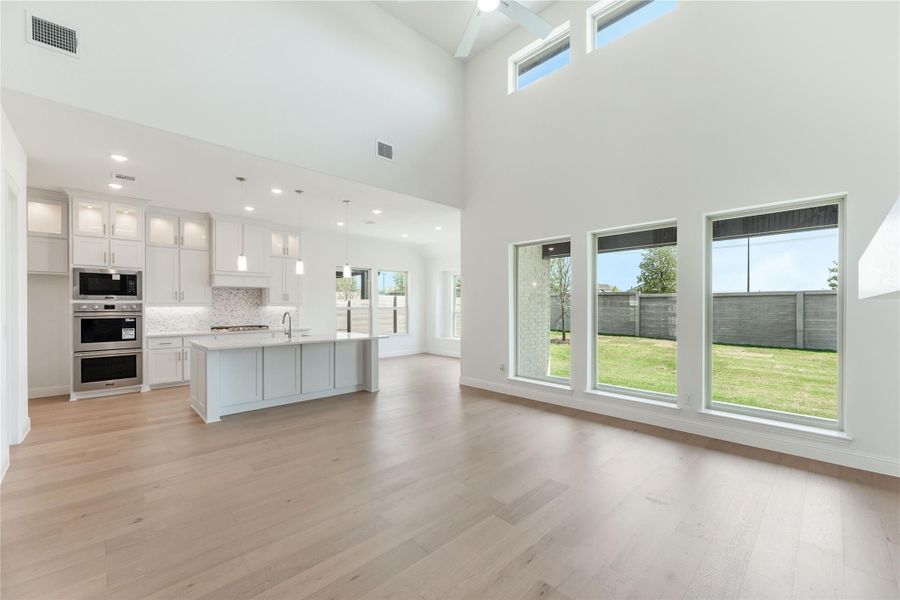 Open living area with high ceilings, hardwood floors, and kitchen island with white cabinets and stainless appliances