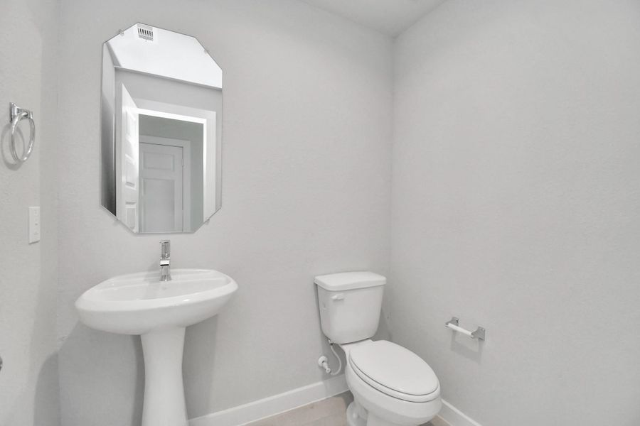 This half bathroom features a stylish pedestal sink, modern hardware, and bright recessed lighting, creating a sleek and inviting space. Sample photo of completed home with similar floor plan. Actual colors and selections may vary.