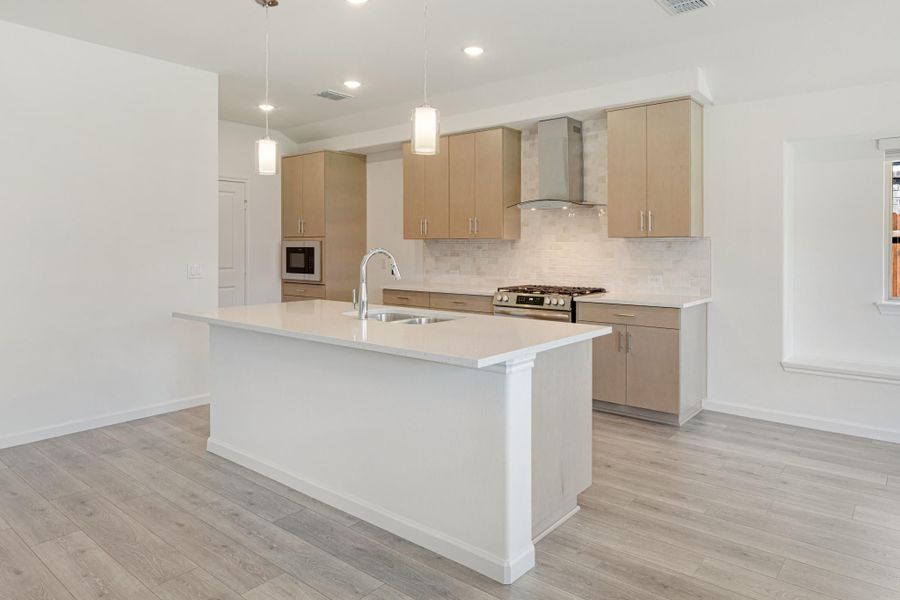 Kitchen with large white island, tan cabinets, stainless steel range, and pendant lights over light wood floors Kitchen with large white island, tan cabinets, stainless steel range, and pendant lights over light wood floors