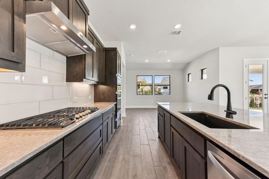 Kitchen with light stone counters, dark brown cabinetry, exhaust hood, recessed lighting, and stainless steel appliances Kitchen with light stone counters, dark brown cabinetry, exhaust hood, recessed lighting, and stainless steel appliances