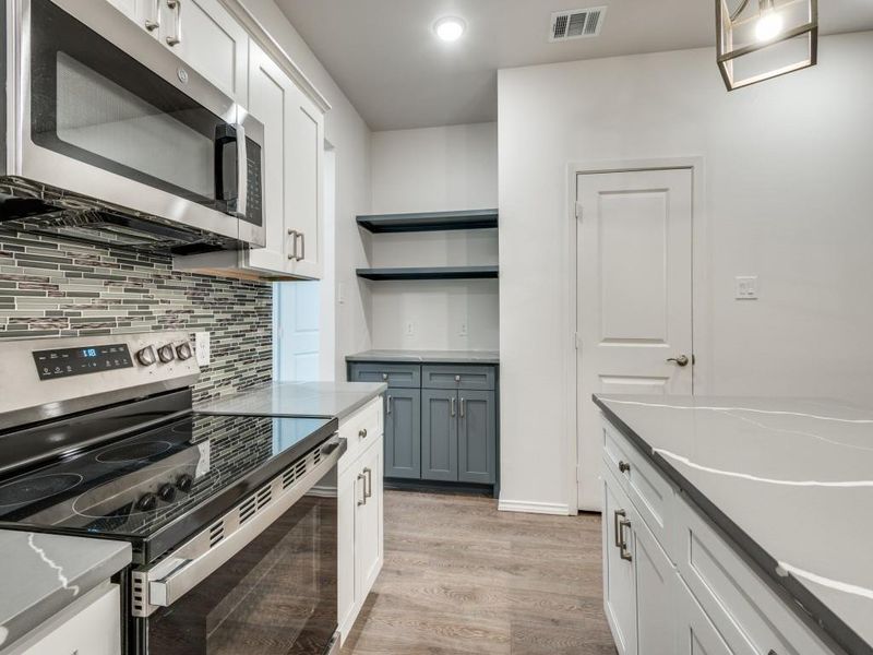 Kitchen with appliances with stainless steel finishes, light hardwood / wood-style floors, white cabinetry, and backsplash