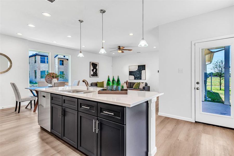 Kitchen with stainless steel dishwasher, sink, light hardwood / wood-style flooring, and an island with sink