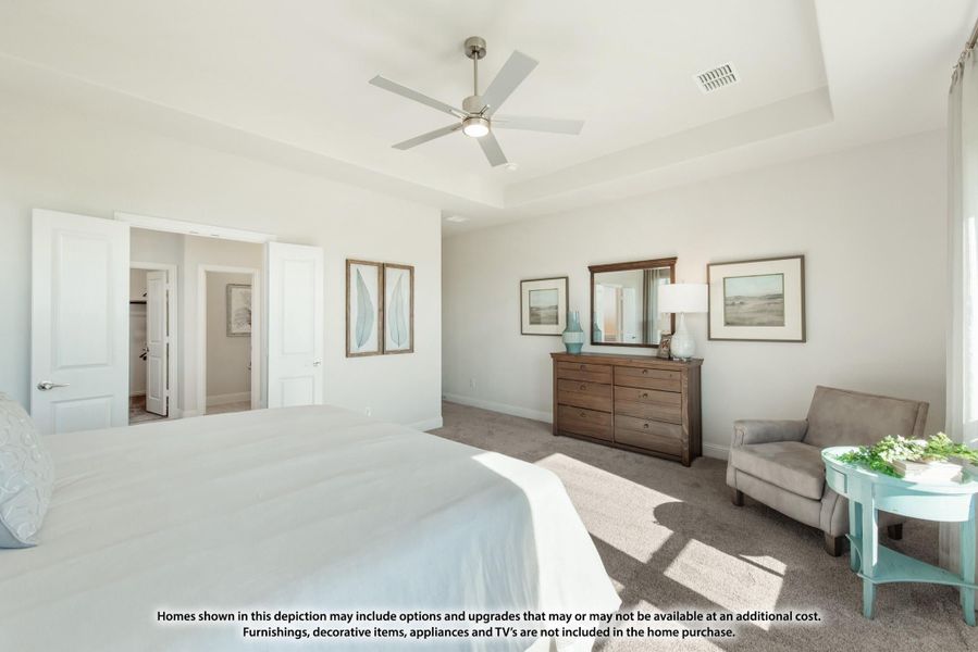Spacious master bedroom with tray ceiling, ceiling fan, wood dresser, and carpet flooring leading to walk-in closet.