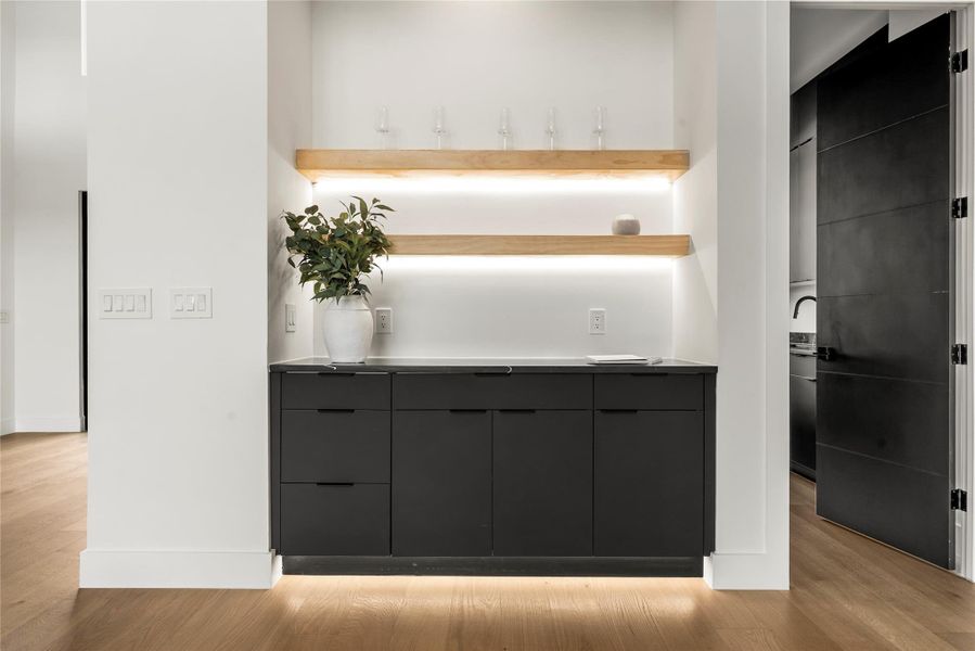 Bar featuring modern cabinets, dark cabinets, stainless steel counters, and light wood-style flooring Bar featuring modern cabinets, dark cabinets, stainless steel counters, and light wood-style flooring