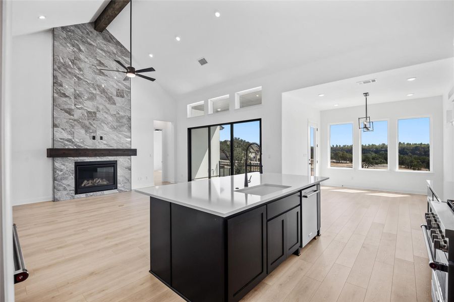 Kitchen with dark cabinetry, open floor plan, a fireplace, light wood-style floors, and a kitchen island with sink