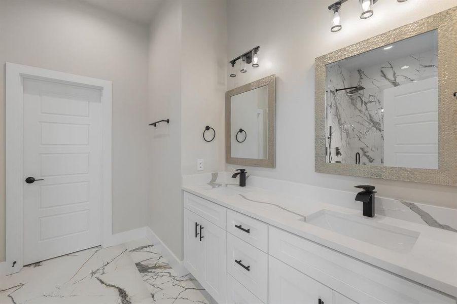 Bathroom featuring a marble finish shower, double vanity, marble finish floors, and baseboards