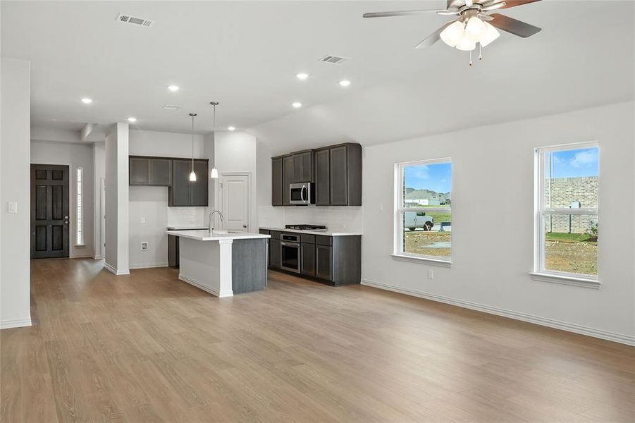 Kitchen featuring a center island with sink, decorative light fixtures, light wood-style floors, open floor plan, and stainless steel appliances Kitchen featuring a center island with sink, decorative light fixtures, light wood-style floors, open floor plan, and stainless steel appliances