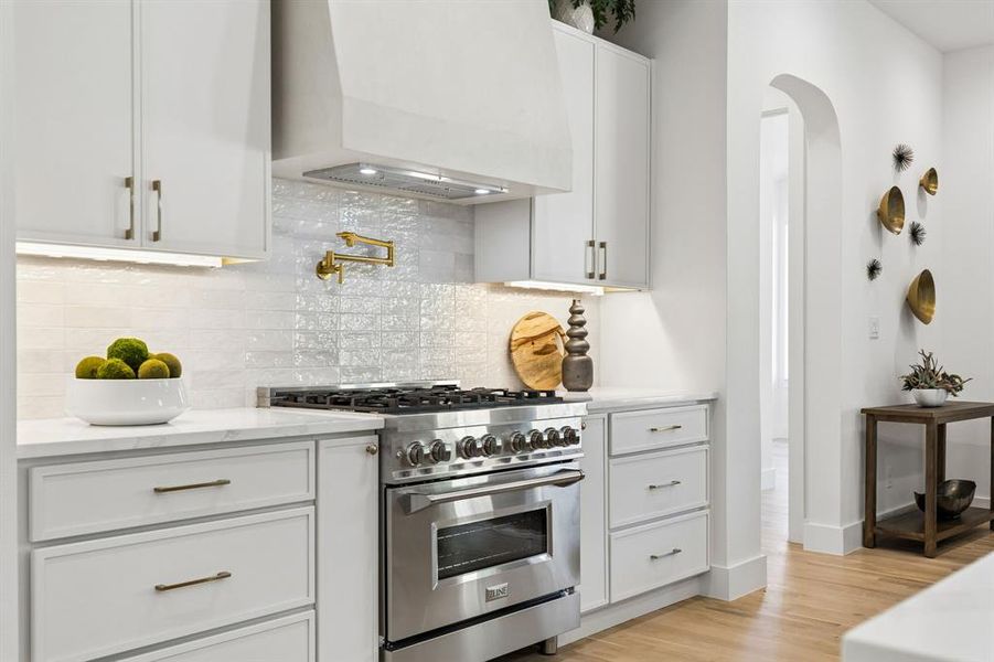 Kitchen featuring high end range, white cabinetry, arched walkways, backsplash, and light wood finished floors