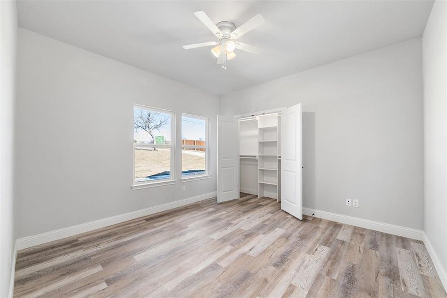 Unfurnished bedroom featuring ceiling fan, a barn door, and light hardwood / wood-style floors