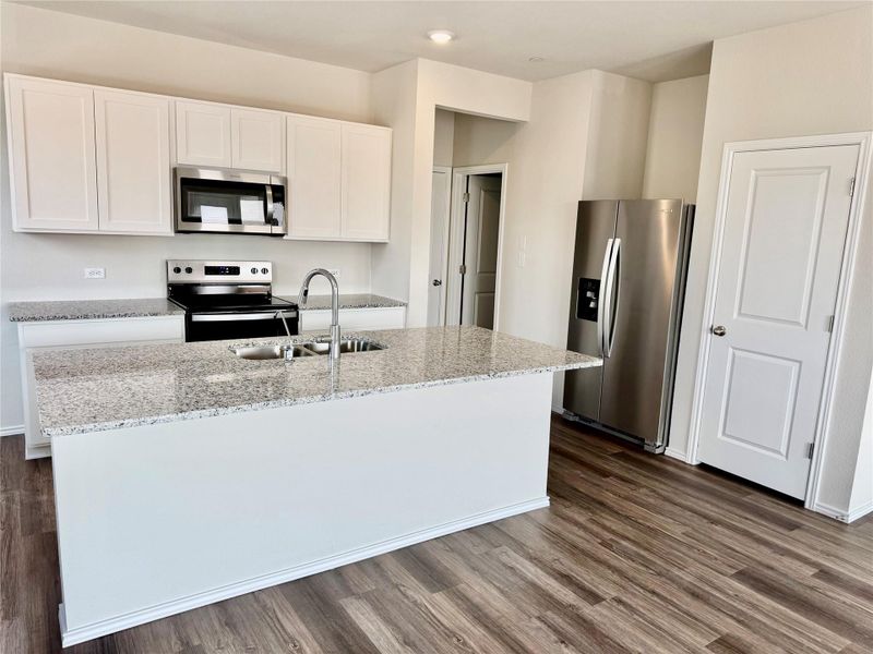 Kitchen with stainless steel appliances, light stone countertops, dark wood-type flooring, white cabinetry, and a kitchen island with sink Kitchen with stainless steel appliances, light stone countertops, dark wood-type flooring, white cabinetry, and a kitchen island with sink