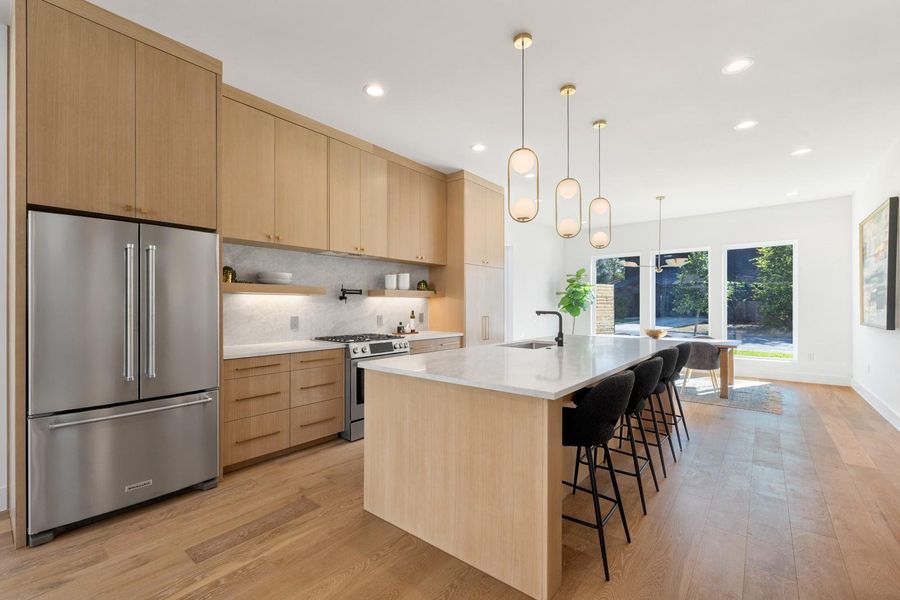 Kitchen featuring appliances with stainless steel finishes, light brown cabinetry, light stone countertops, open shelves, and hanging light fixtures Kitchen featuring appliances with stainless steel finishes, light brown cabinetry, light stone countertops, open shelves, and hanging light fixtures