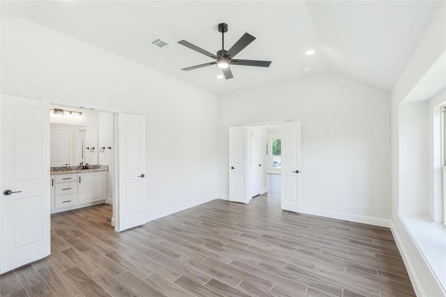 Empty master bedroom with vaulted ceiling, ceiling fan, wood-look floors, and ensuite bathroom access Empty master bedroom with vaulted ceiling, ceiling fan, wood-look floors, and ensuite bathroom access