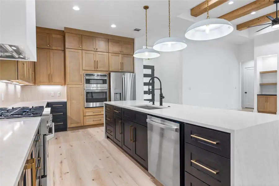 Kitchen with light quartz countertops, light wood-style floors, stainless steel appliances, premium range hood, and solid wood cabinets Kitchen with light quartz countertops, light wood-style floors, stainless steel appliances, premium range hood, and solid wood cabinets