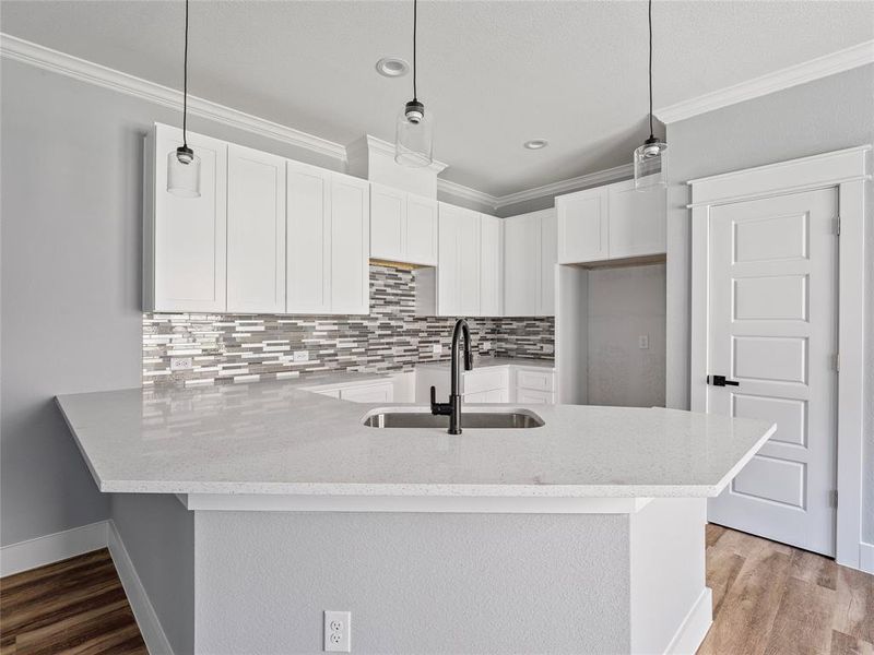 Kitchen featuring crown molding, a peninsula, a sink, light stone counters, and tasteful backsplash