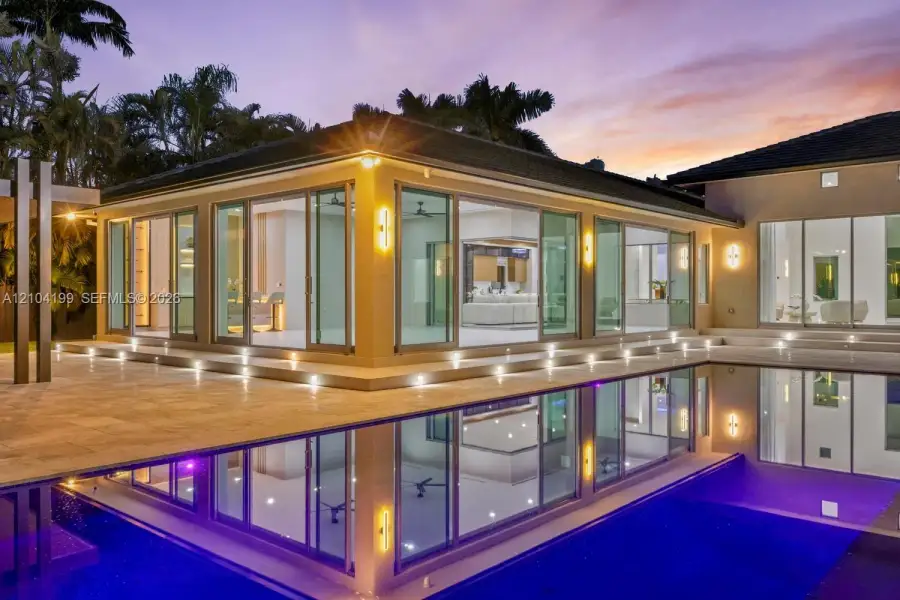 Contemporary exterior featuring floor-to-ceiling sliding glass doors, integrated ground-level accent lighting, stone-tiled patio, and a recessed swimming pool