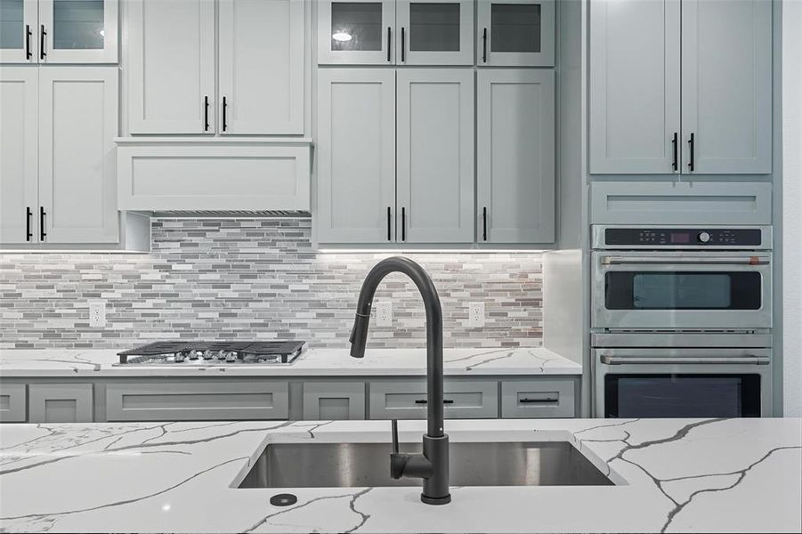 Kitchen featuring glass insert cabinets, light stone countertops, and backsplash Kitchen featuring glass insert cabinets, light stone countertops, and backsplash