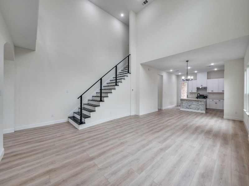 Unfurnished living room featuring stairs, a chandelier, light wood finished floors, baseboards, and recessed lighting