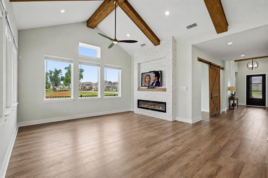 This sleek and stylish electric fireplace serves as a stunning focal point in the Family Room, showcasing a dramatic floor-to-ceiling stacked stone surround accented by a custom wood mantel. Thoughtfully designed to complement the rich tones of the LVP flooring, the feature creates a cohesive and sophisticated aesthetic throughout the space. The mantel is prewired for a television, offering effortless entertainment setup.