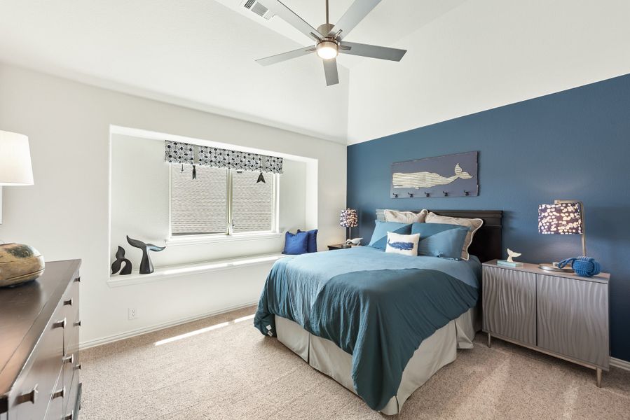 Bedroom with blue accent wall, ceiling fan, window seat, and carpeted floor