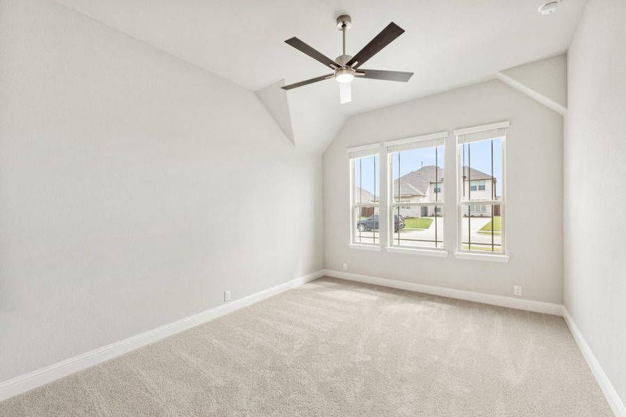 Empty bedroom with vaulted ceiling, ceiling fan, carpet flooring, and three windows with neighborhood view