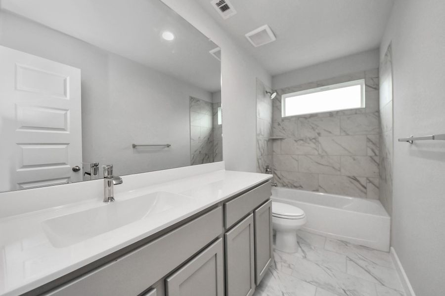 Secondary bath features tile flooring, bath/shower combo with tile surround, light stainedwood cabinets, beautiful light countertop.