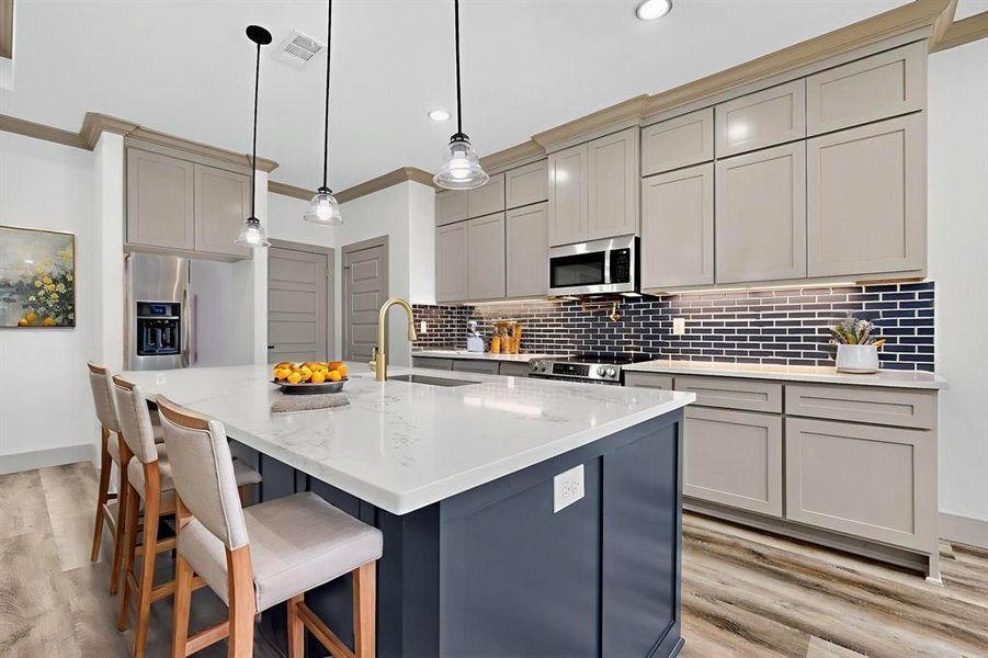 Kitchen featuring gray cabinetry, backsplash, a kitchen island with sink, light stone counters, and crown molding